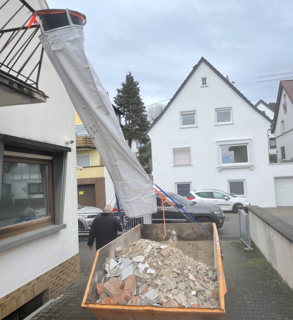 Goulotte à gravats flexible installée depuis un balcon vers une benne pour évacuer des gravats de rénovation