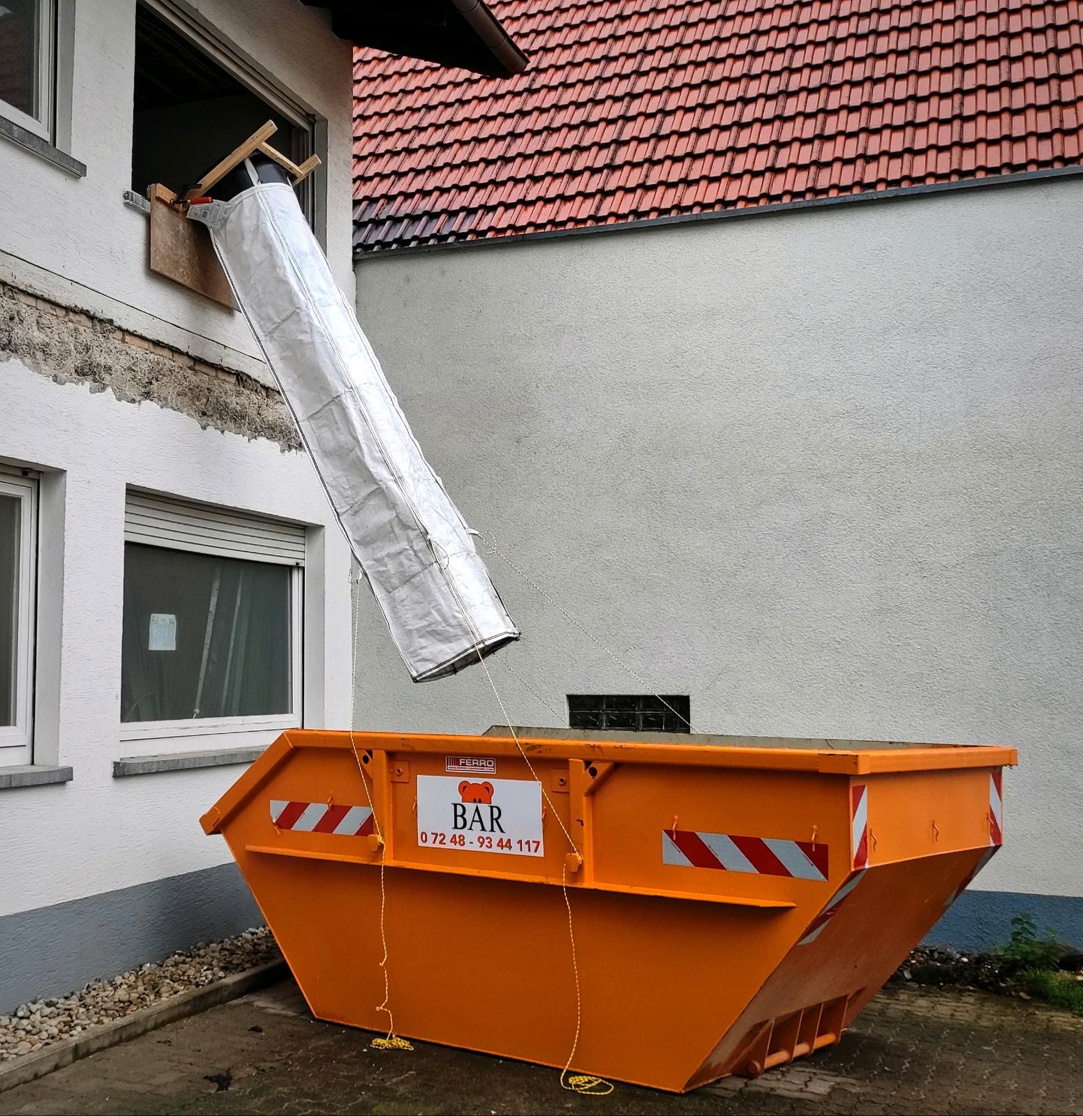 Goulotte à gravats flexible sortant d’une fenêtre vers une benne pour rénovation de façade